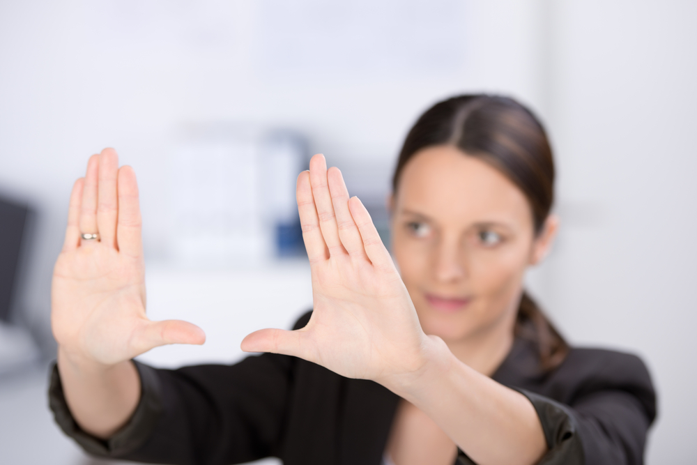 Mid adult businesswoman making hand frame in office, focus hands